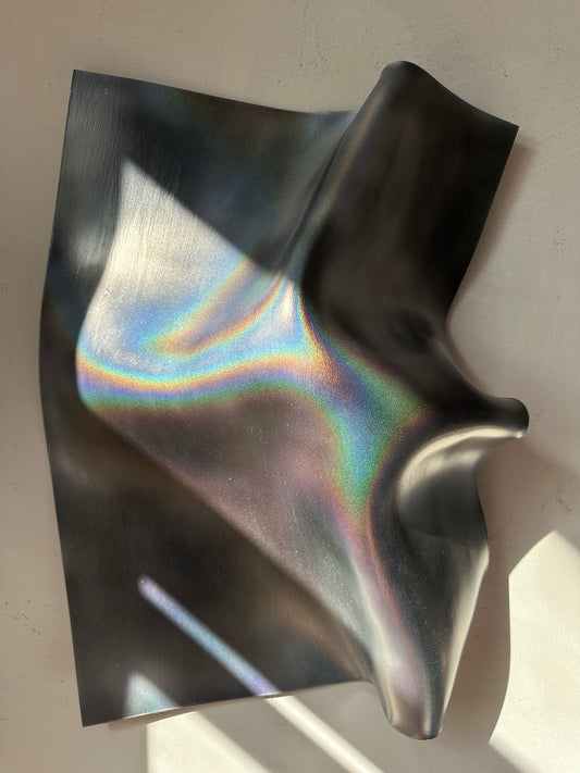 Dark, iridescent wall sculpture with a metallic, holographic finish, draped to show its reflective properties against a neutral background.