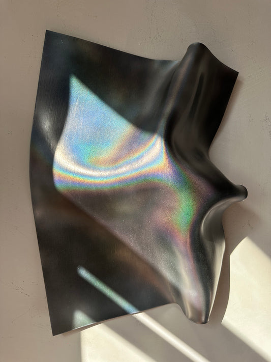 Holographic wall sculpture draped to show a rainbow-colored reflective pattern against a light gray background.