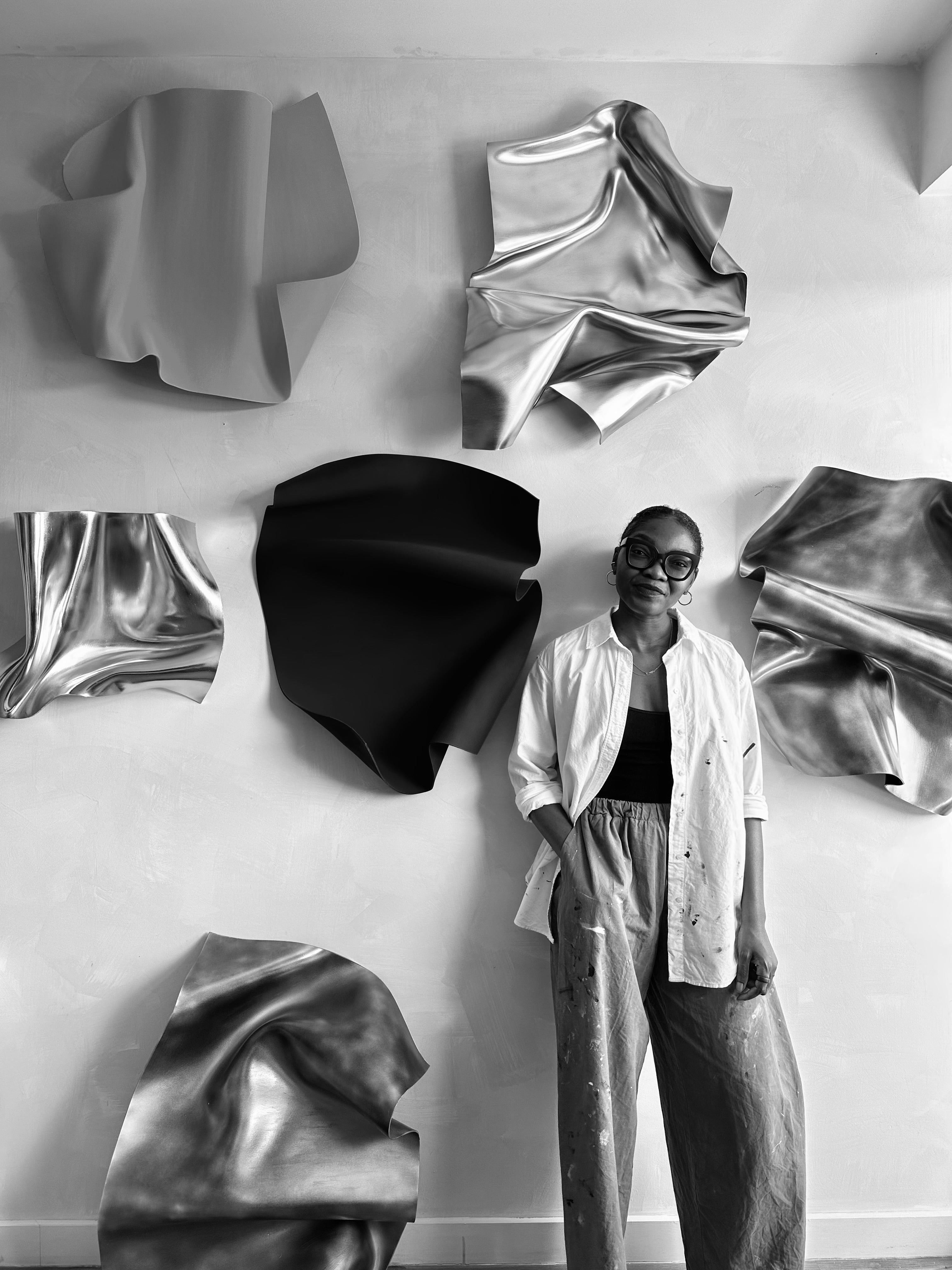Artist standing in front of abstract wall sculptures in a modern interior setting